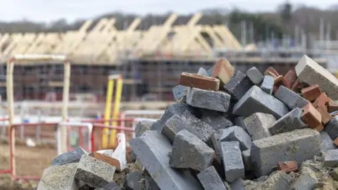 Bloomberg via Getty Images A pile of bricks on a building site with houses being constructed in the background