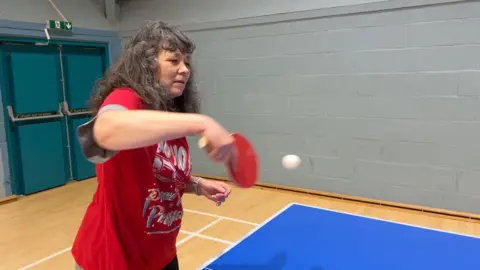 BBC A woman in a red Christmas top returns the ball during a table tennis session organised by Sport in Mind.