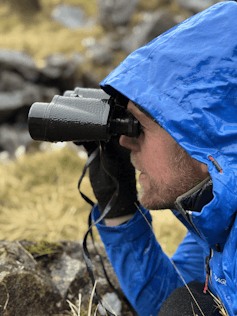man in bllue coat looks through binoculars