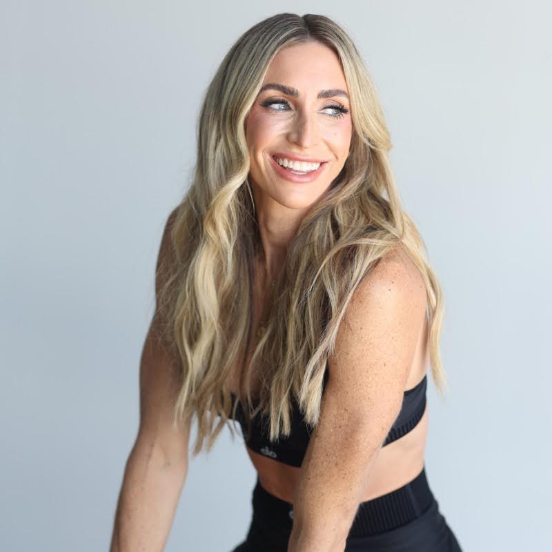 Patty Brewton wears a sports bra and leggings and smiles at something off camera.