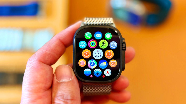 An individual holding an Apple Watch in their left hand, the watch is displaying apps in a honeycomb-like grid