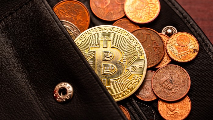 A bitcoin token among euro coins in a partially open black wallet.