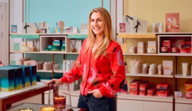 Nicola Elliott stands smiling in the NEOM wellbeing store, surrounded by NEOM products on display shelves.