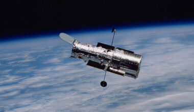 Image of a cylindrical telescope orbiting above a cloudy Earth.