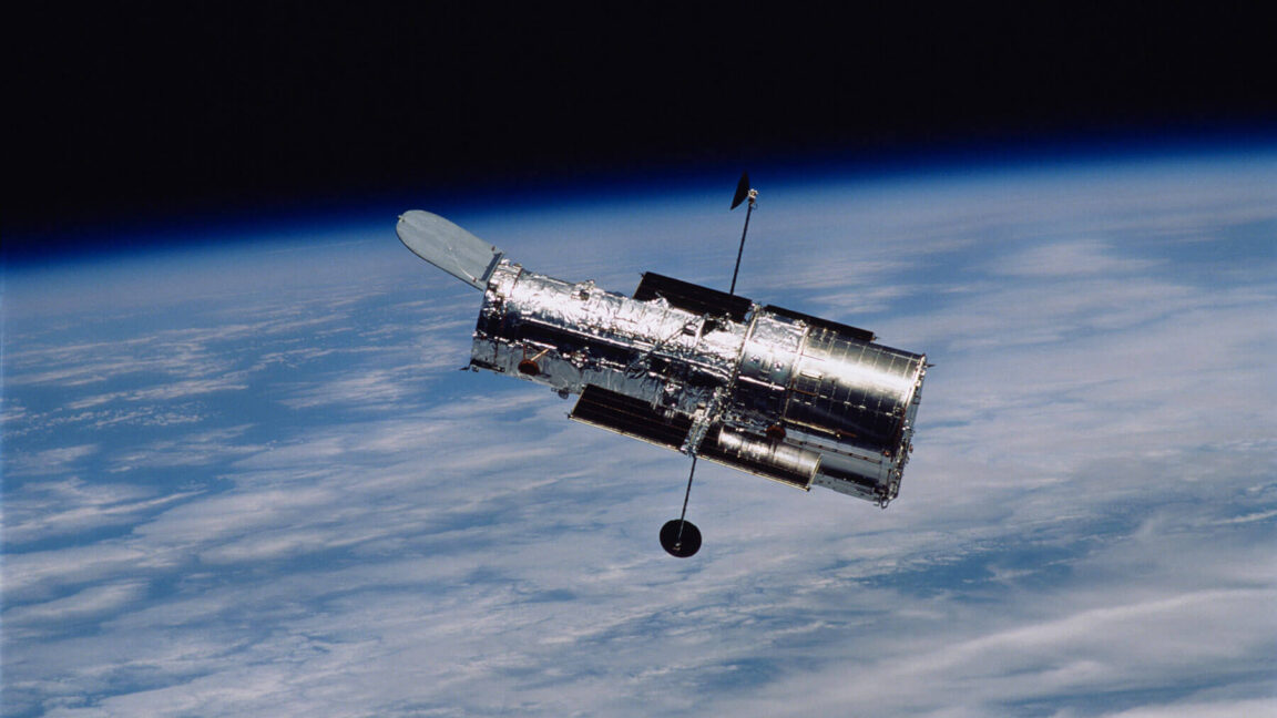 Image of a cylindrical telescope orbiting above a cloudy Earth.