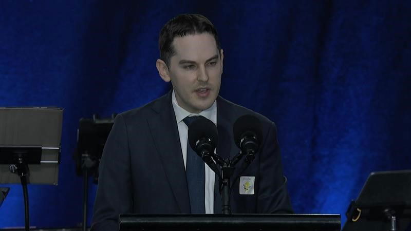A man wearing a suit speaks into a mic at a podium