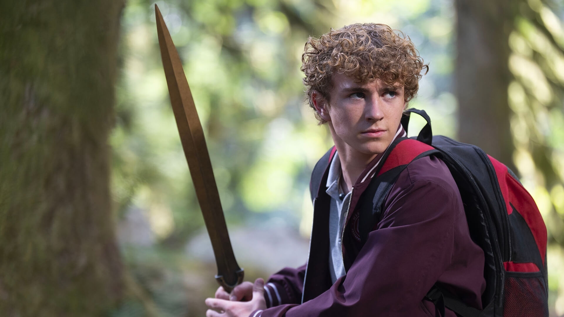 Percy holding a sword and wearing a backpack in Percy Jackson and the Olympians.