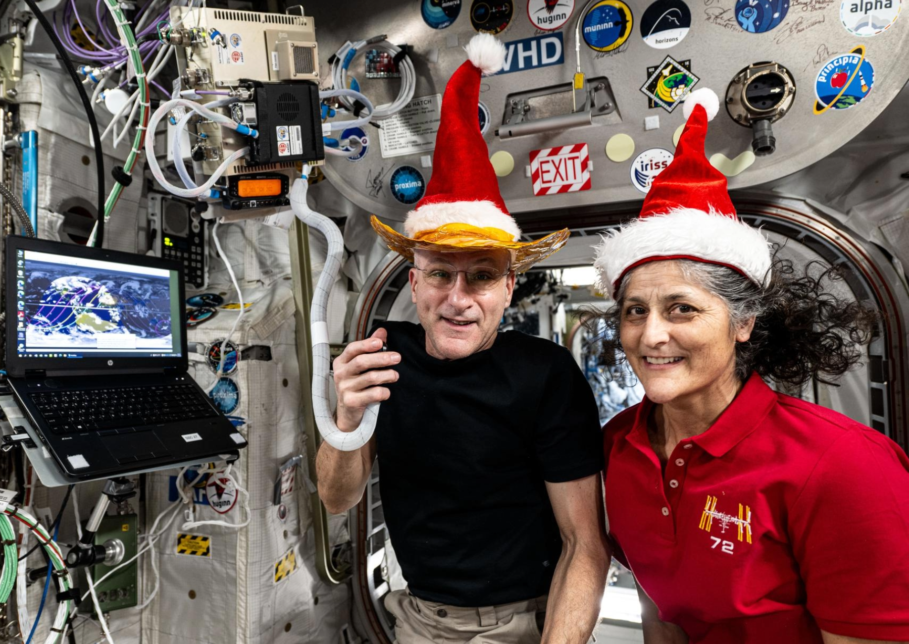 two astronauts operate a hame radio while wearing santa hats