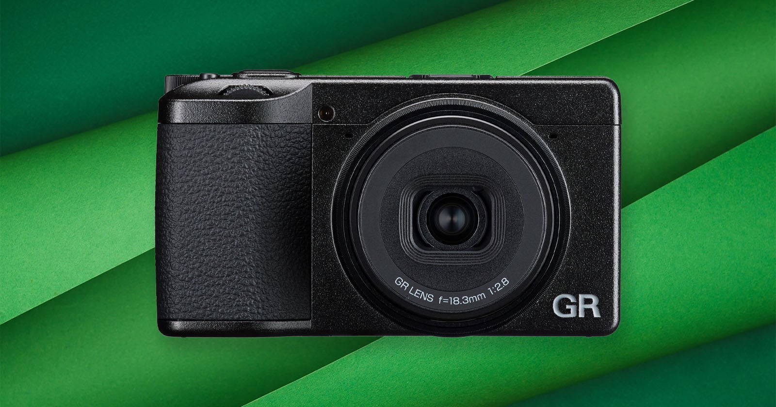 A compact black digital camera with a prominent GR lens is centered on a background of overlapping green paper strips.