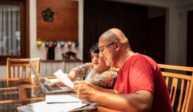 Two people looking at paperwork while sitting at a laptop.