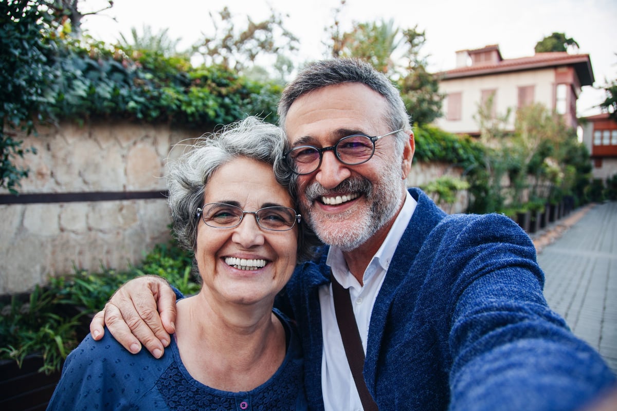 A couple wearing blue is outdoors, smiling for a selfie.