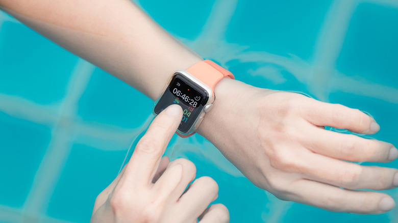 A closeup of someone with an Apple Watch on their wrist, and it is halfway submerged underwater. The individual is tapping something on the still-active screen.