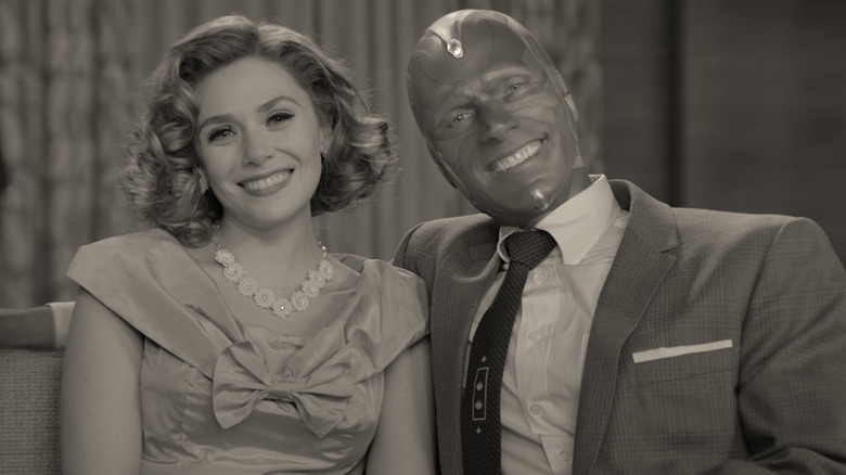 Vision (Paul Bettany) and Wanda (Elizabeth Olsen) smiling while sitting on a couch on WandaVision