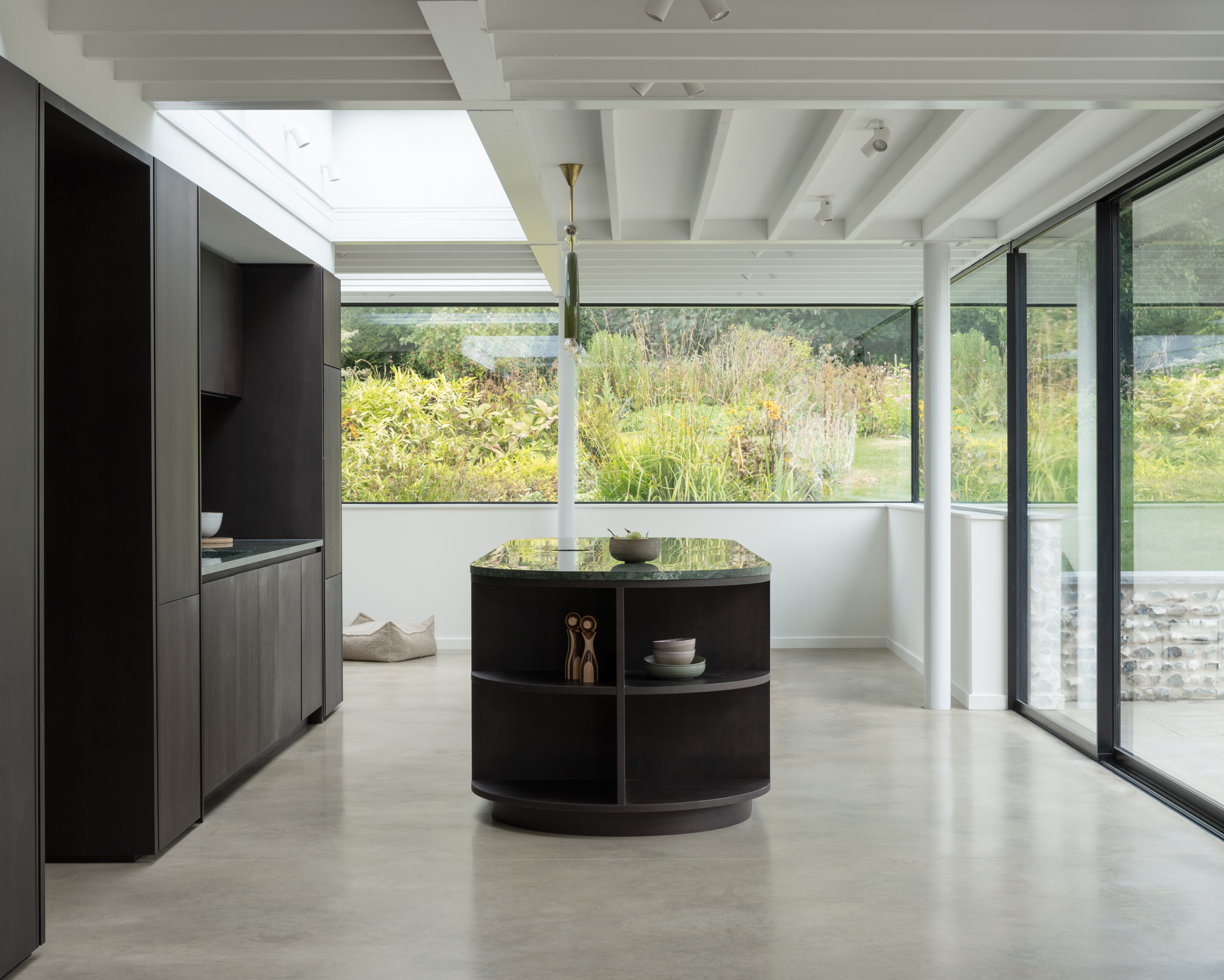 Modern kitchen with dark cabinetry, a dark green marble island, and large windows overlooking a garden.