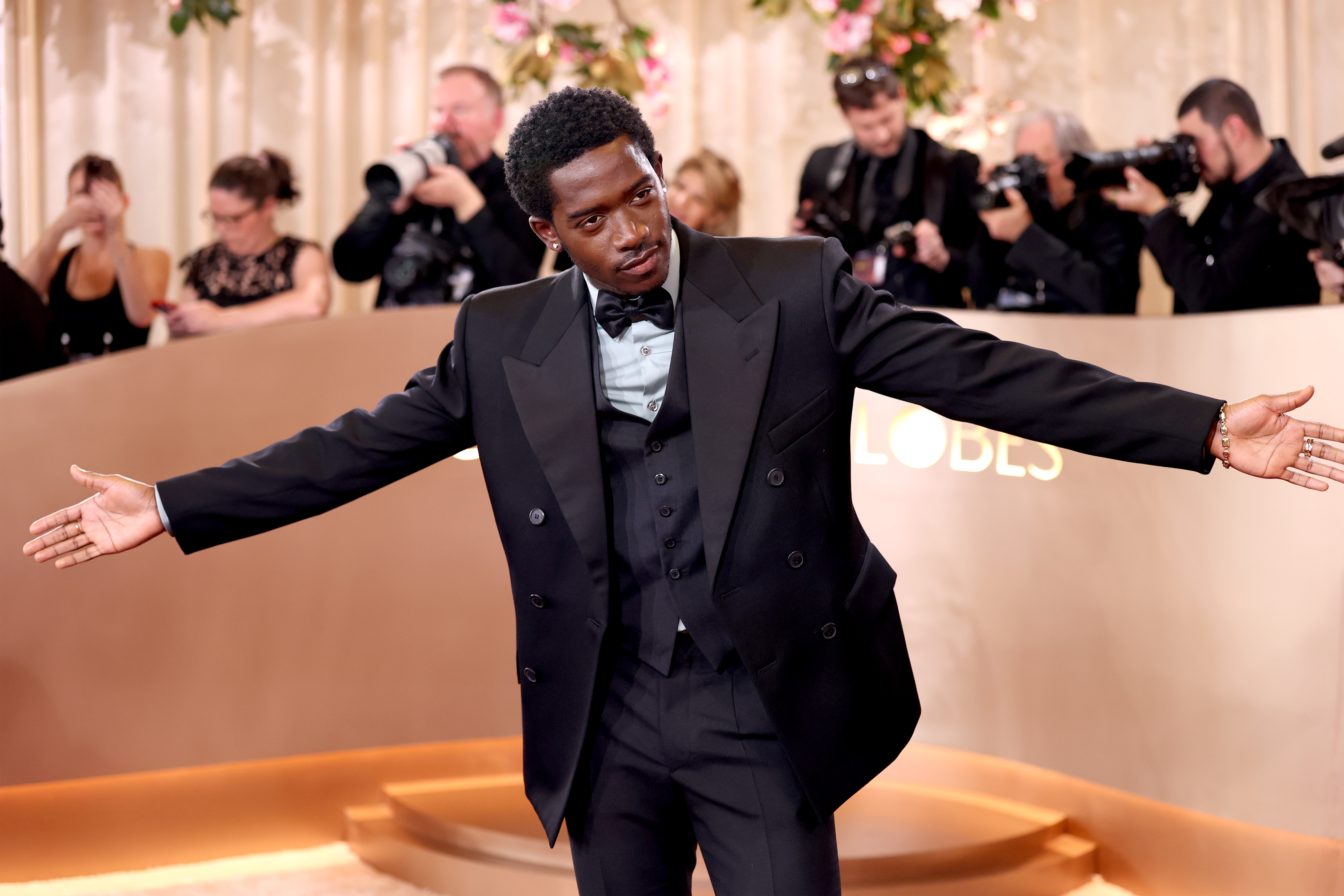 Damson Idris in a black suit with his arms outstretched at the 83rd Annual Golden Globe Awards.