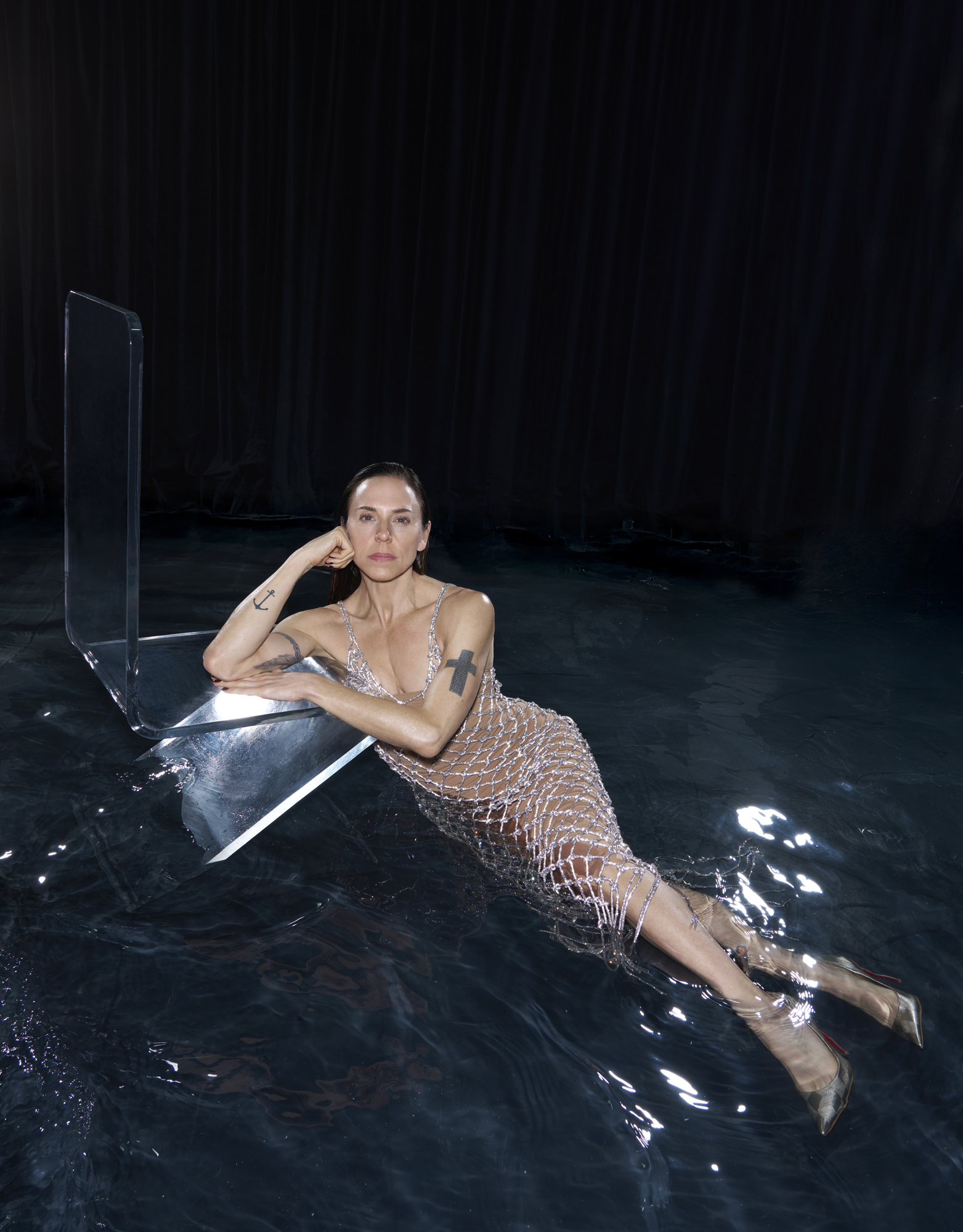 Melanie Chisholm in a silver net dress, leaning on a clear surface in dark water for a Sunday Times STYLE cover shoot.