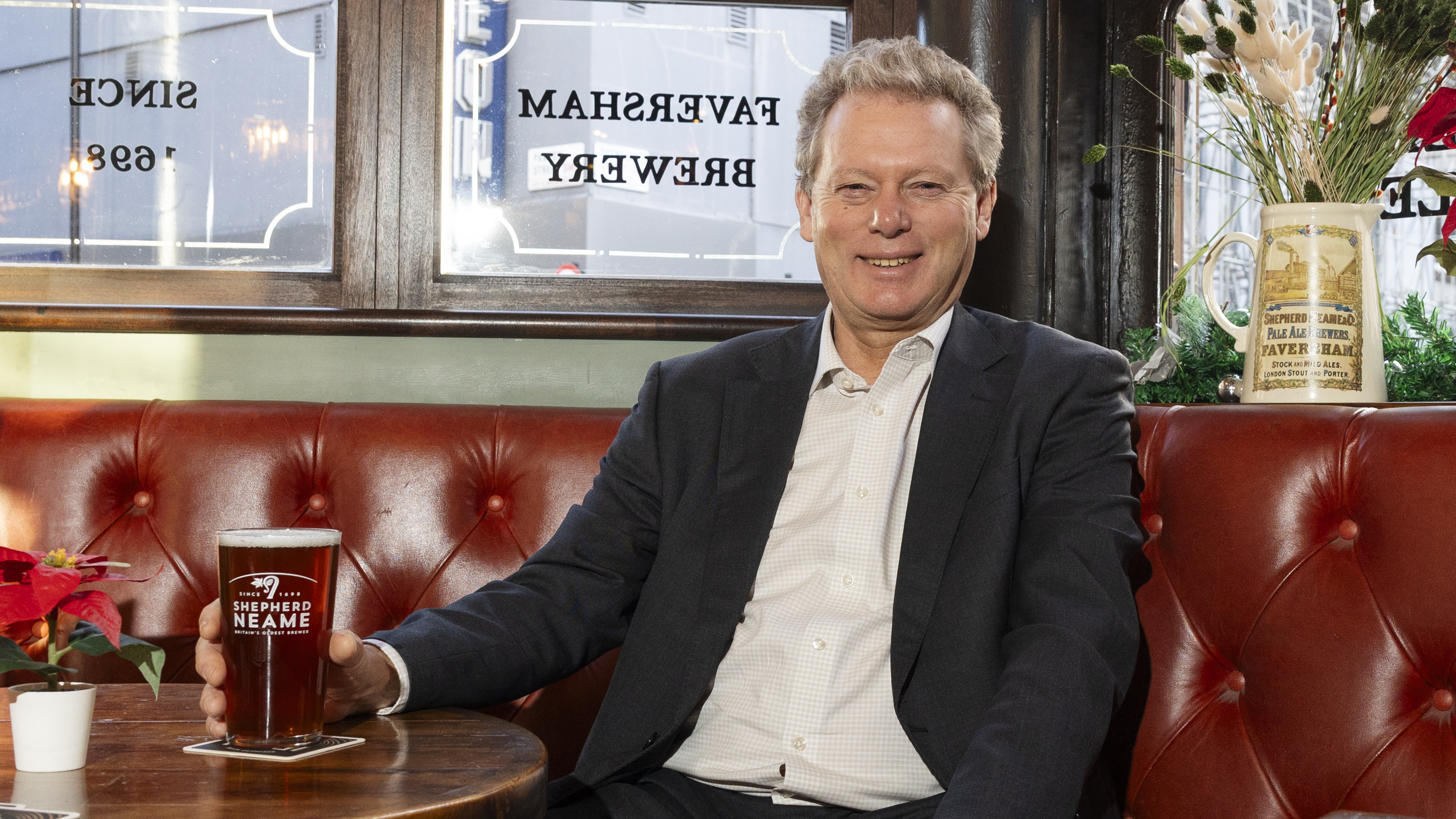 Jonathan Neame, CEO of Shepherd Neame, smiling and holding a pint of beer inside The Thomas Cribb pub.