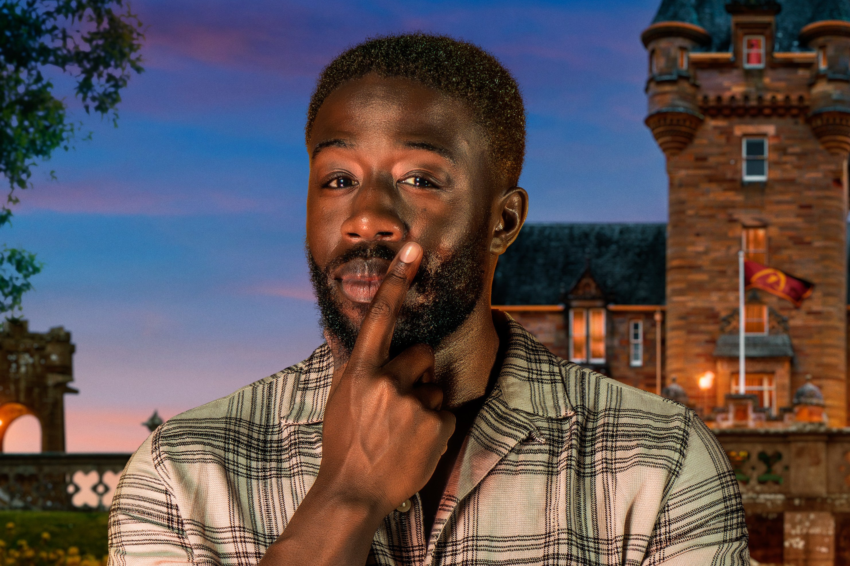 Ross, a contestant from BBC's The Traitors, poses with a finger to his lips, in front of a castle and fire pits.