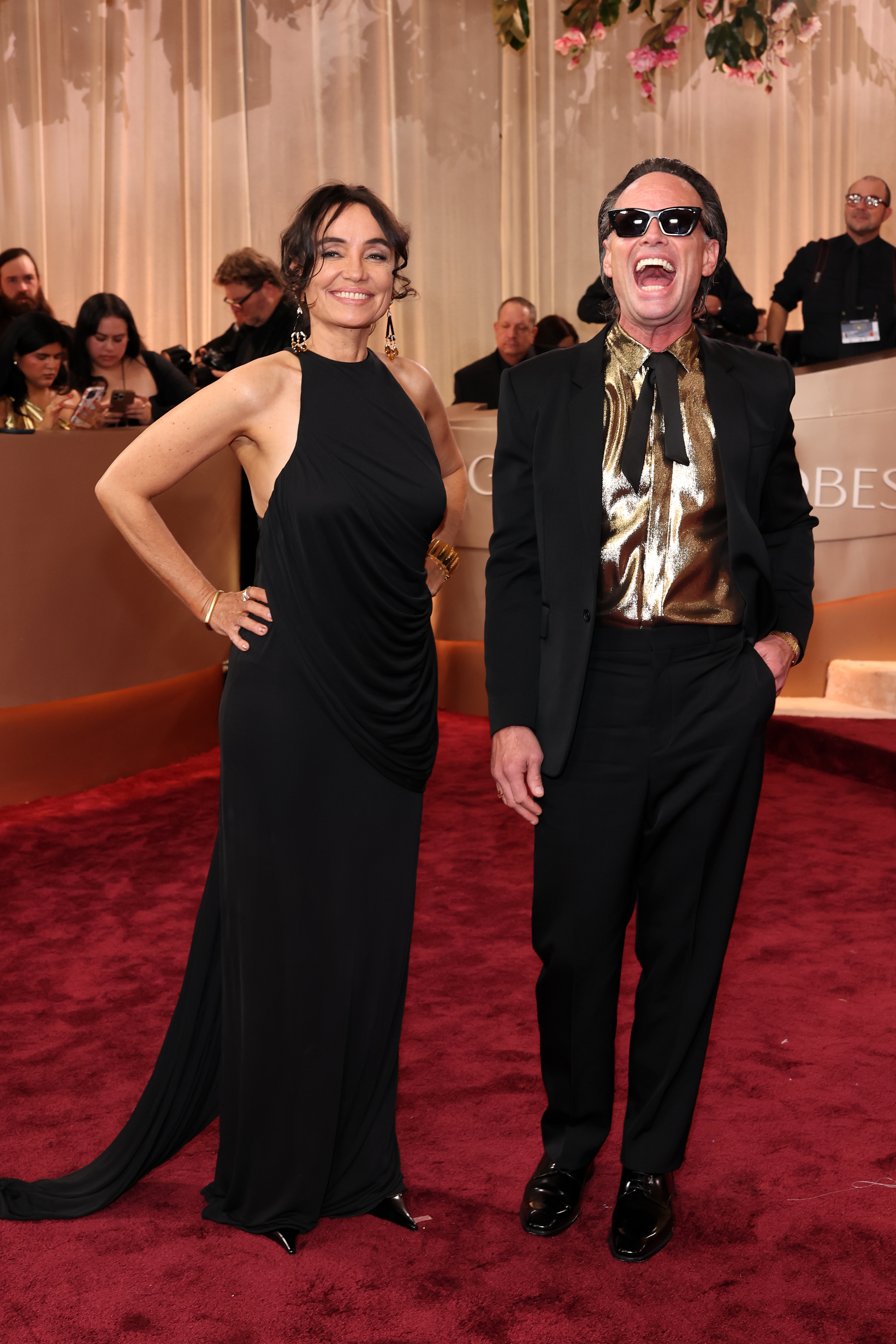 Nadia Conners in a black halter dress and Walton Goggins in a black suit with a gold shirt attend the 83rd Annual Golden Globe Awards.