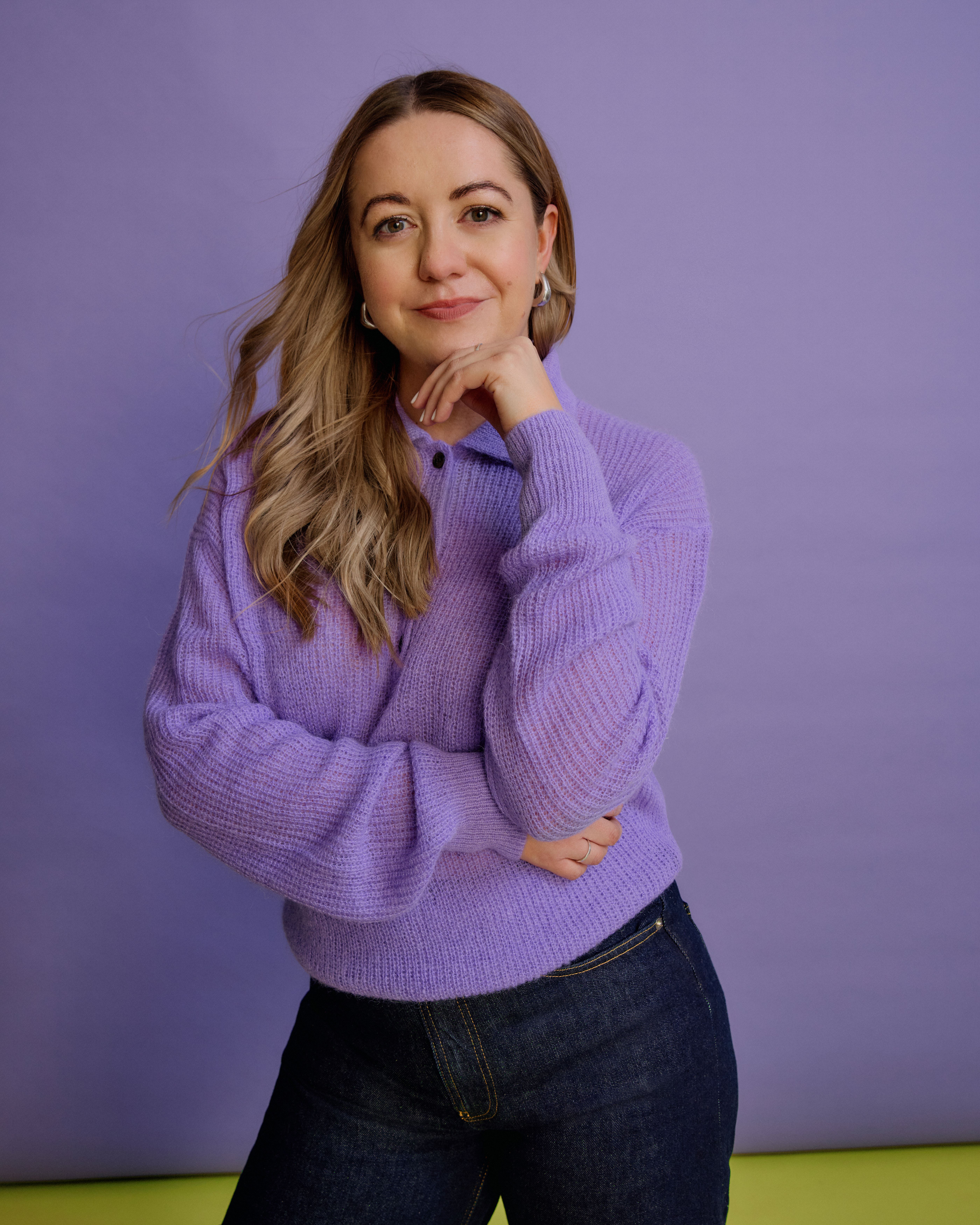 Franky Rousell with blonde hair and a purple sweater, posing with her hand to her chin.