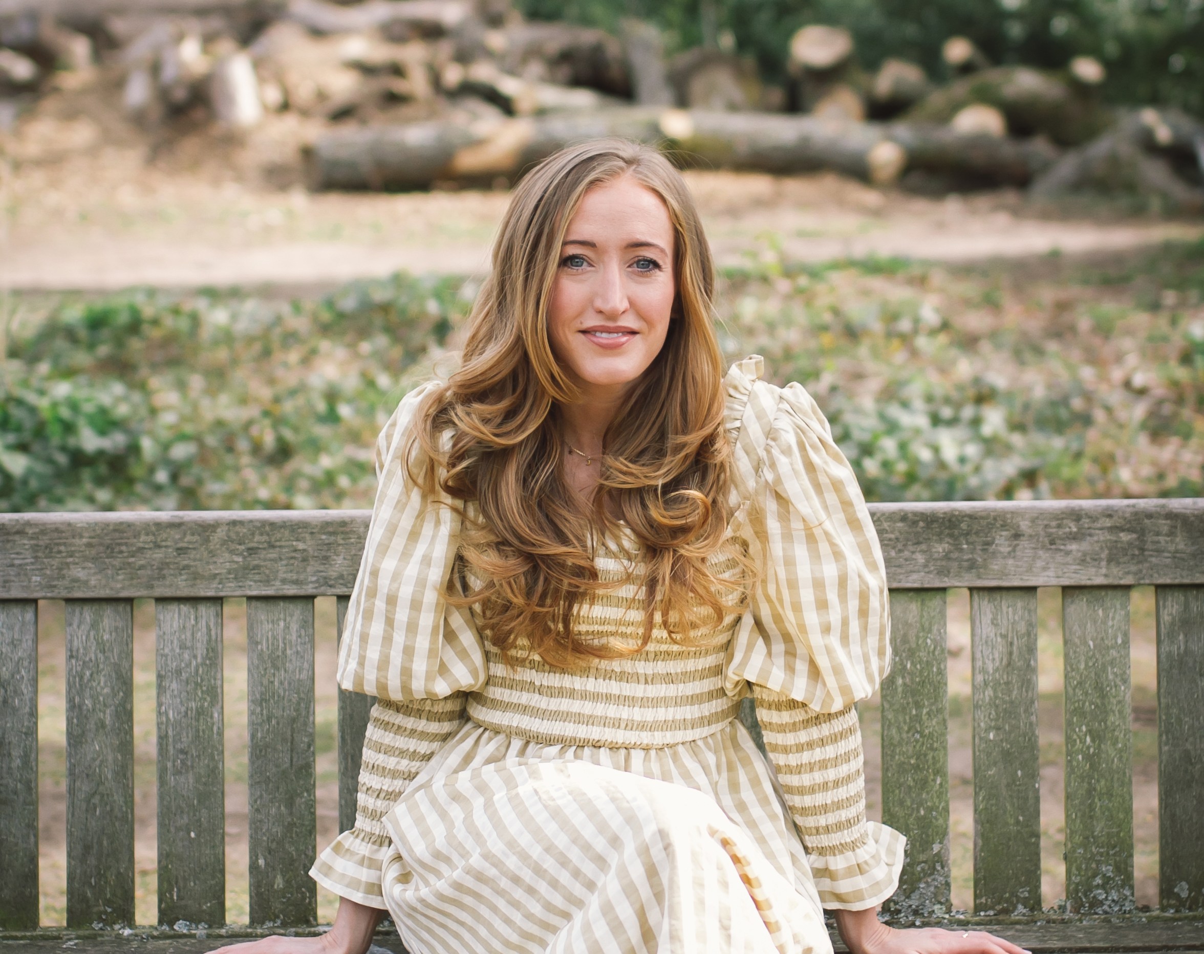Lucy Upton seated on a wooden bench, smiling at the camera.