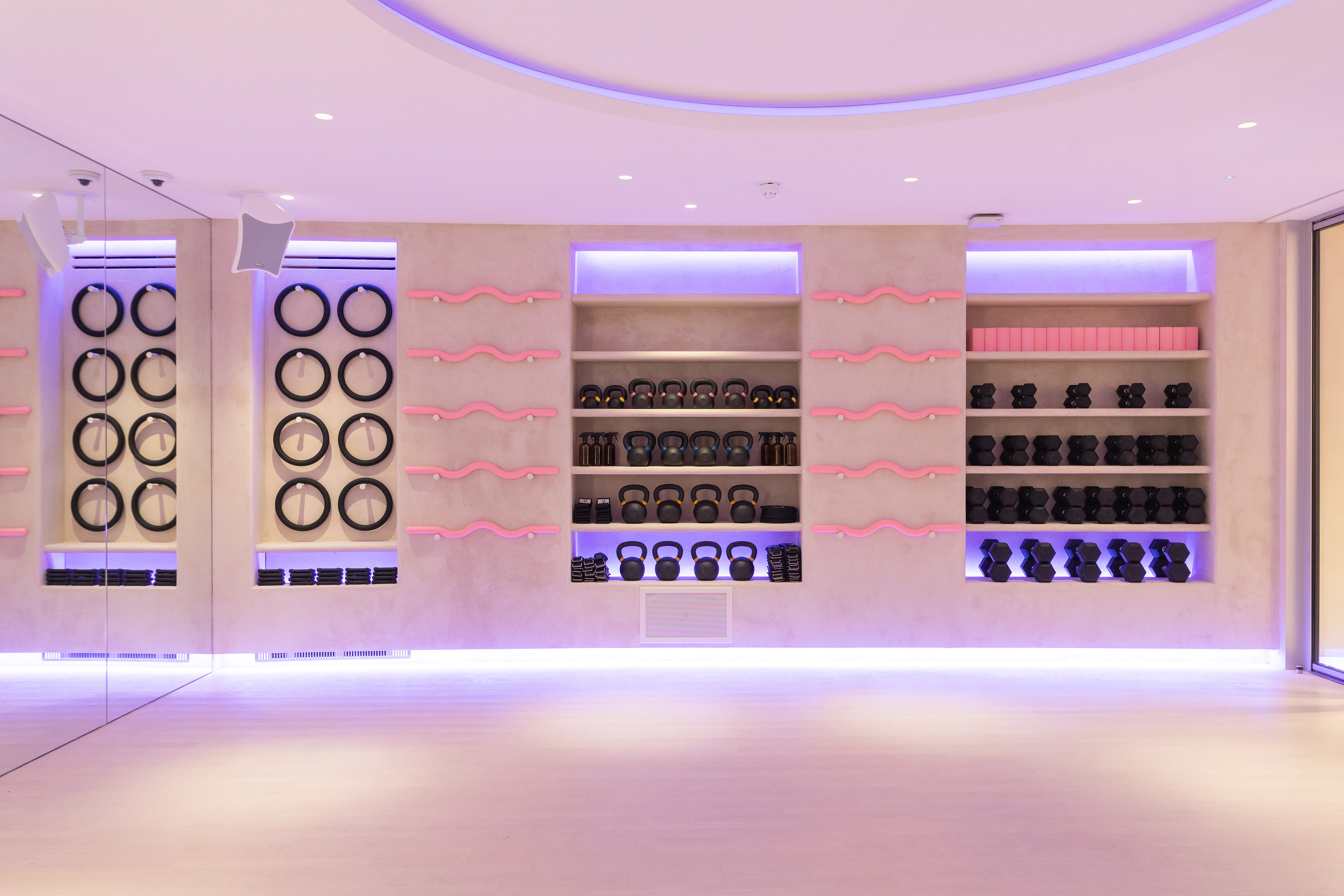 Studio fitness room with kettlebells, dumbbells, and resistance bands on shelves.