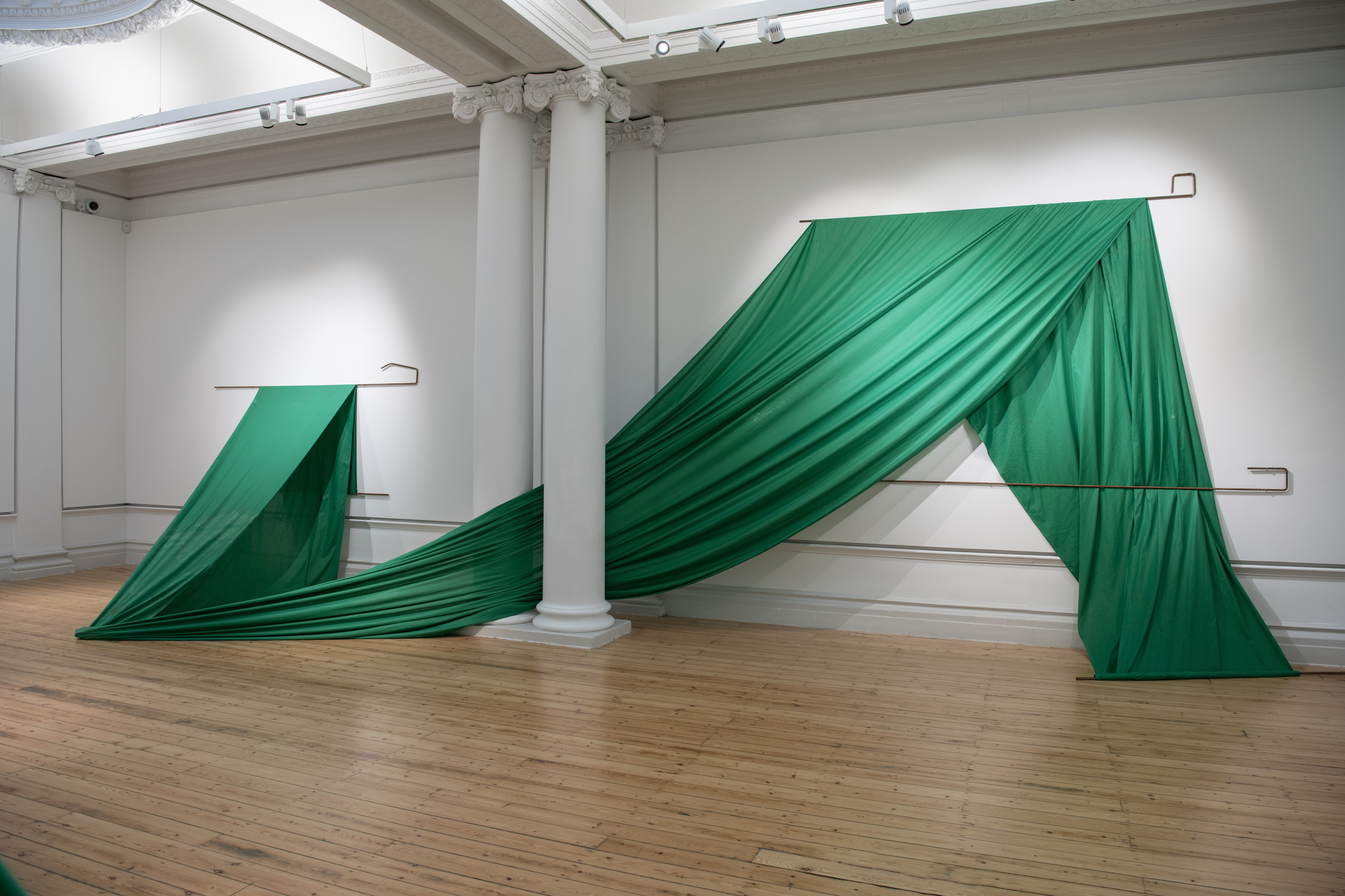 Green fabric draped between two poles against a white wall with columns.