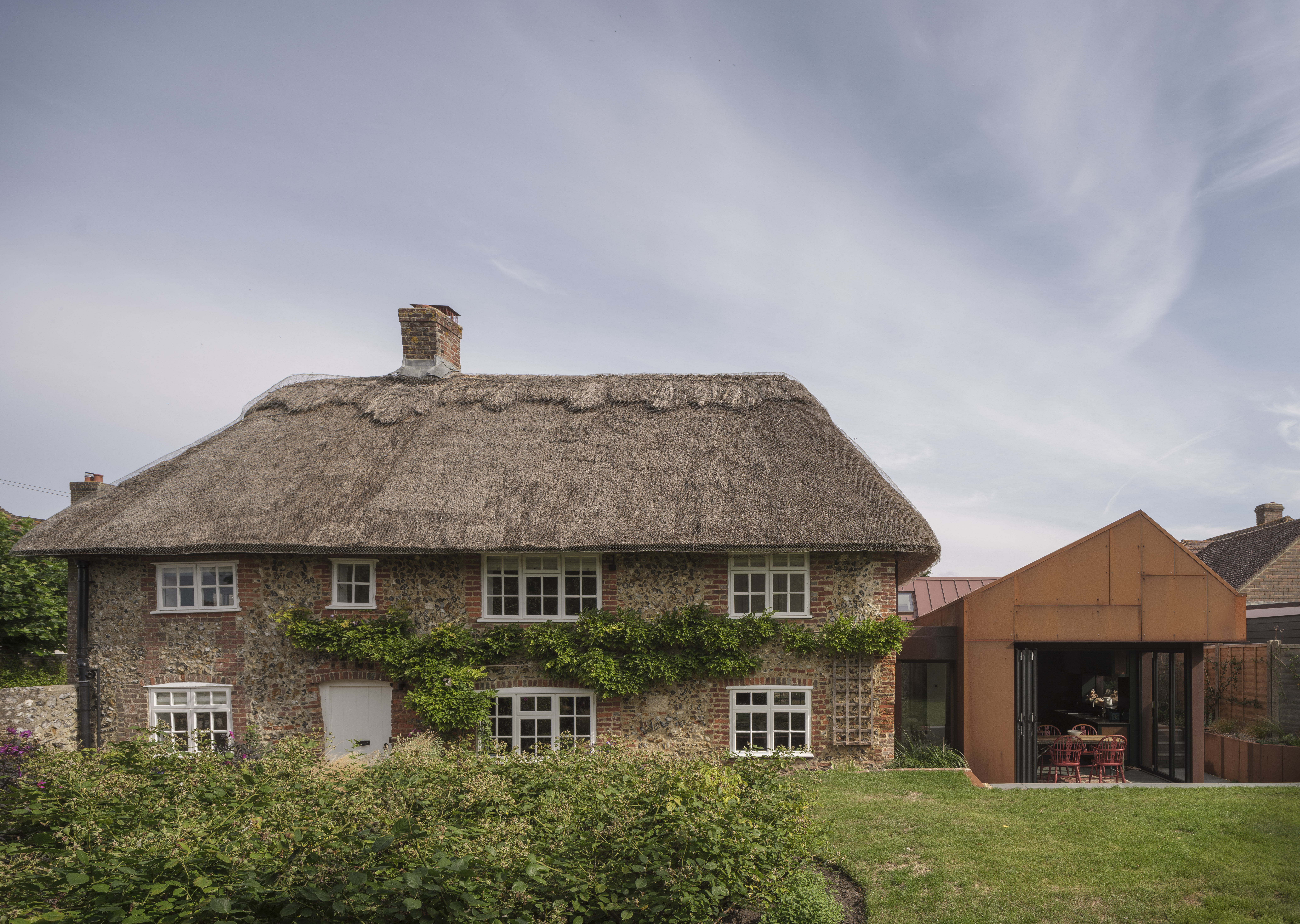 Laurel Cottage, a historic home with a thatched roof, brick and stone walls, and a new modern extension with copper cladding.