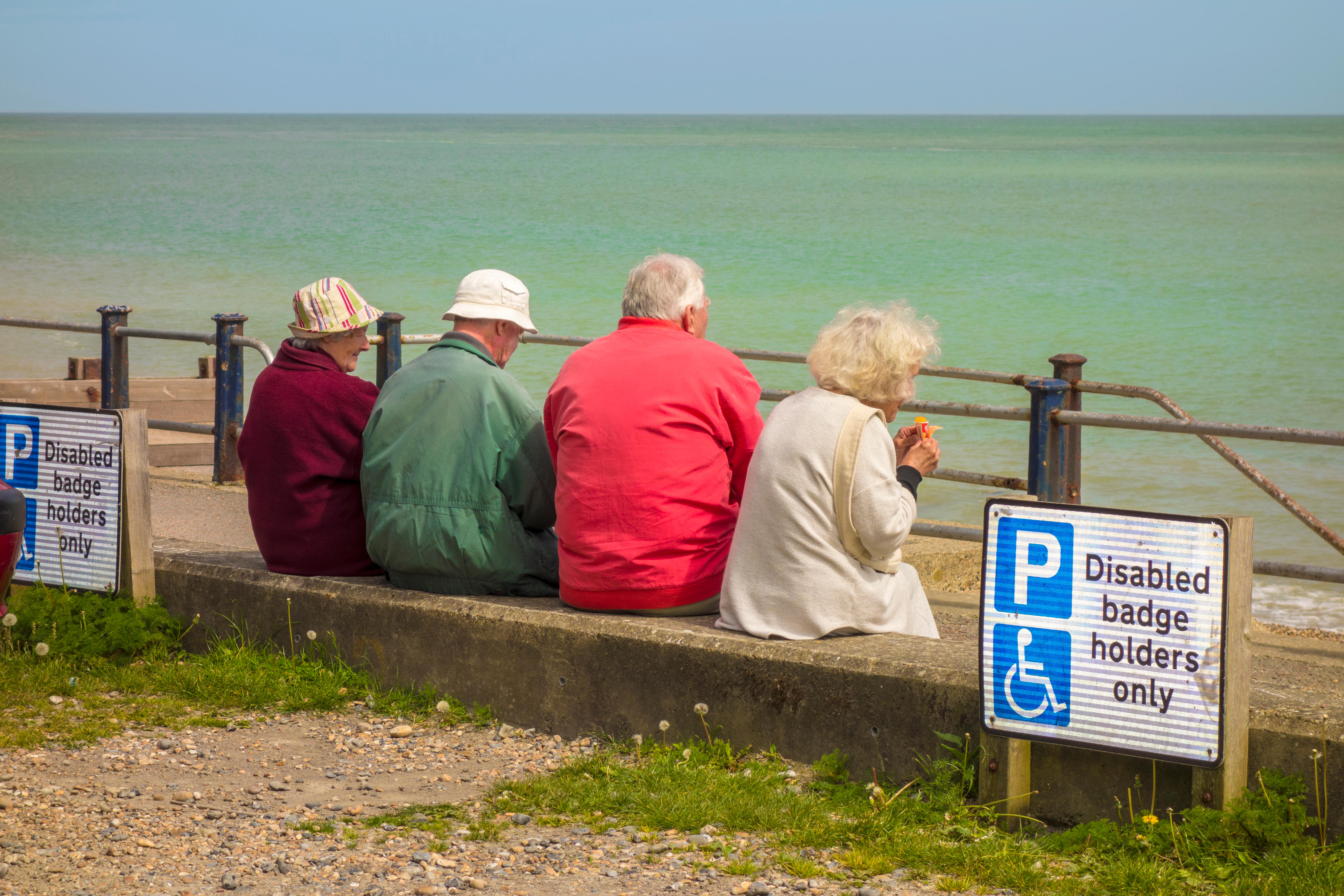Four seniors sitting by the sea enjoying the view, with one holding an ice cream.