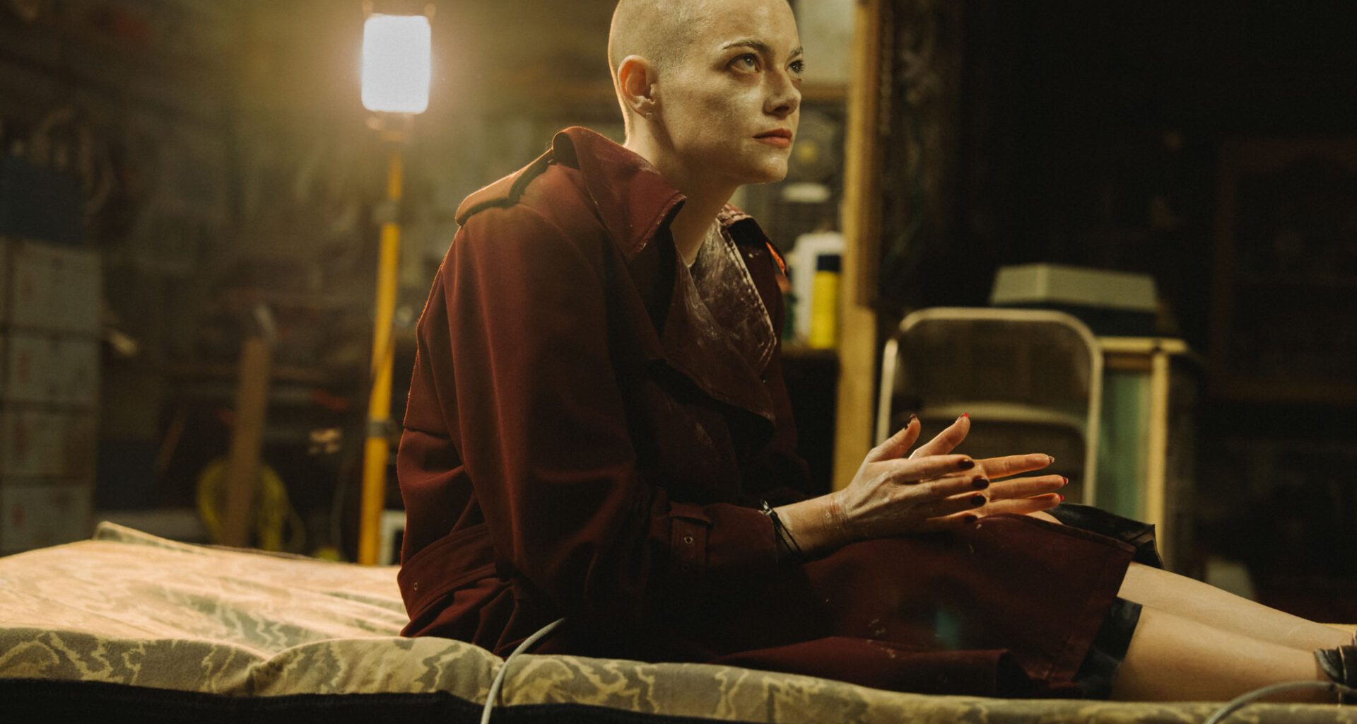 A character named Varang, portrayed by Oona Chaplin, features striking face paint and intricate accessories, set in a dramatic lighting typical of the 20th Century Studios' film 'Avatar: Fire and Ash.' The background includes shadowy figures, highlighting the character's fierce expression.