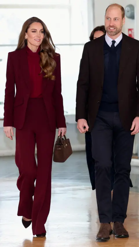 PA Media Catherine, who wore her hair down and carried a small handbag, was dressed in a burgundy trouser suit with matching blouse, while William wore a v neck jumper over his shirt and tie, with his suit jacket.