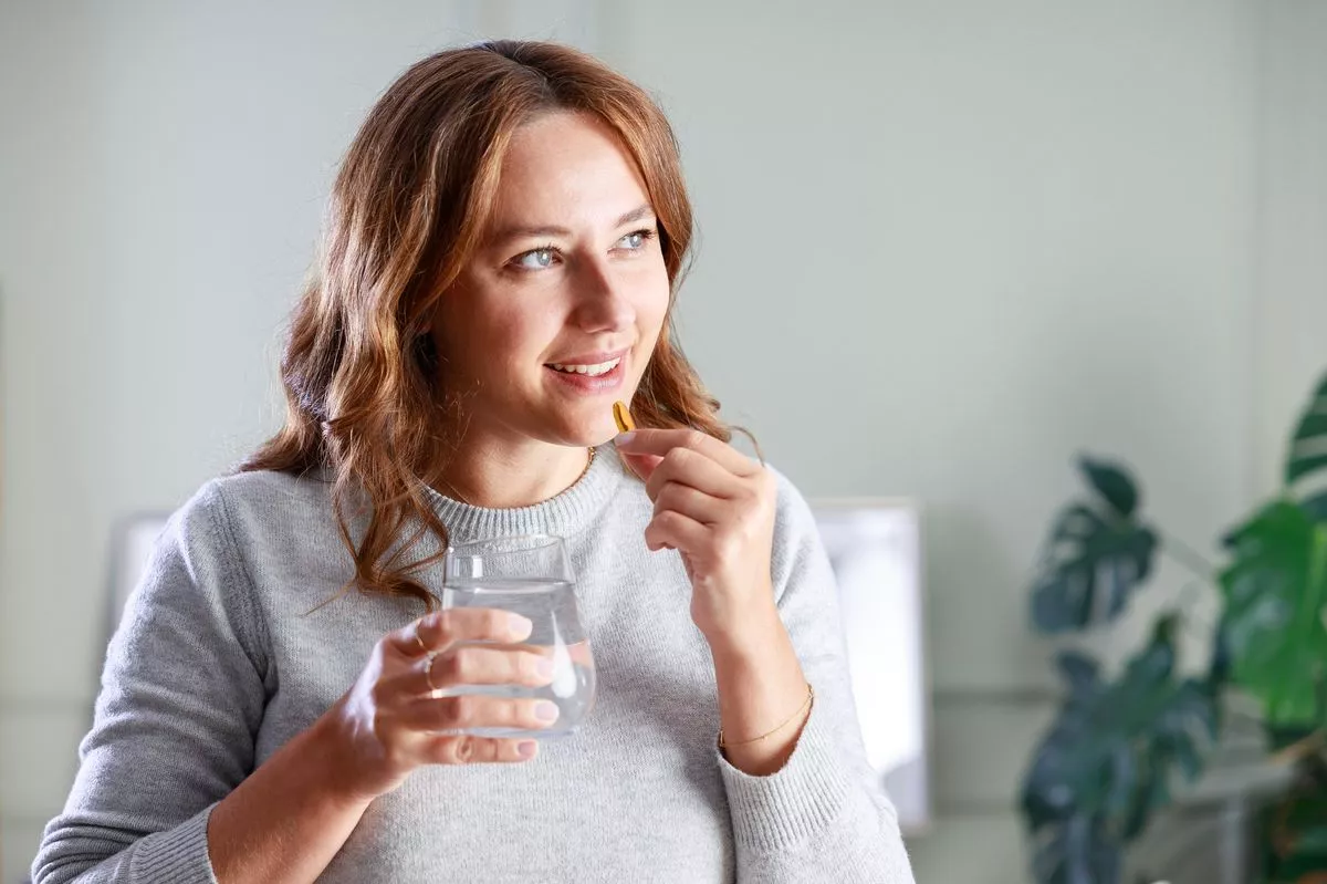 Happy young woman taking omega 3 capsule