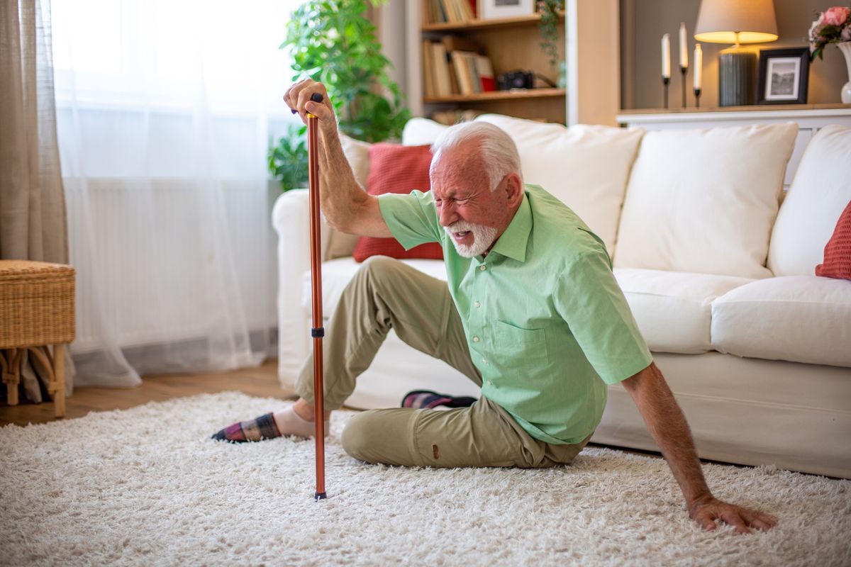 Elderly man falling down at home, holding his cane and shouting in pain
