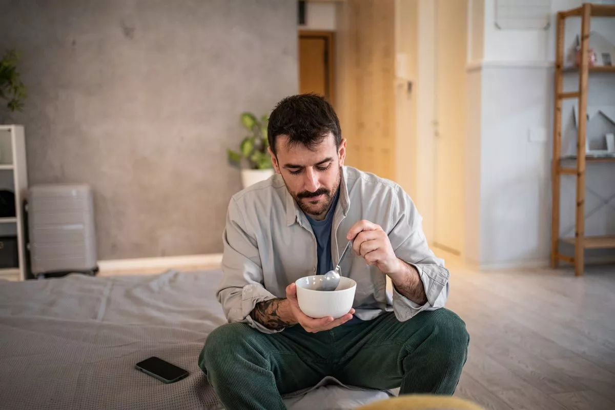  Man eating cereal while sitting on a bed
