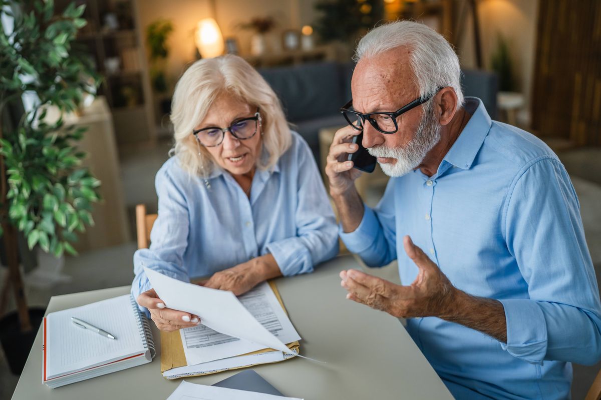 Senior couple looking at documents and making a stressful phone call, managing bills and expenses together while dealing with frustrating administrative tasks