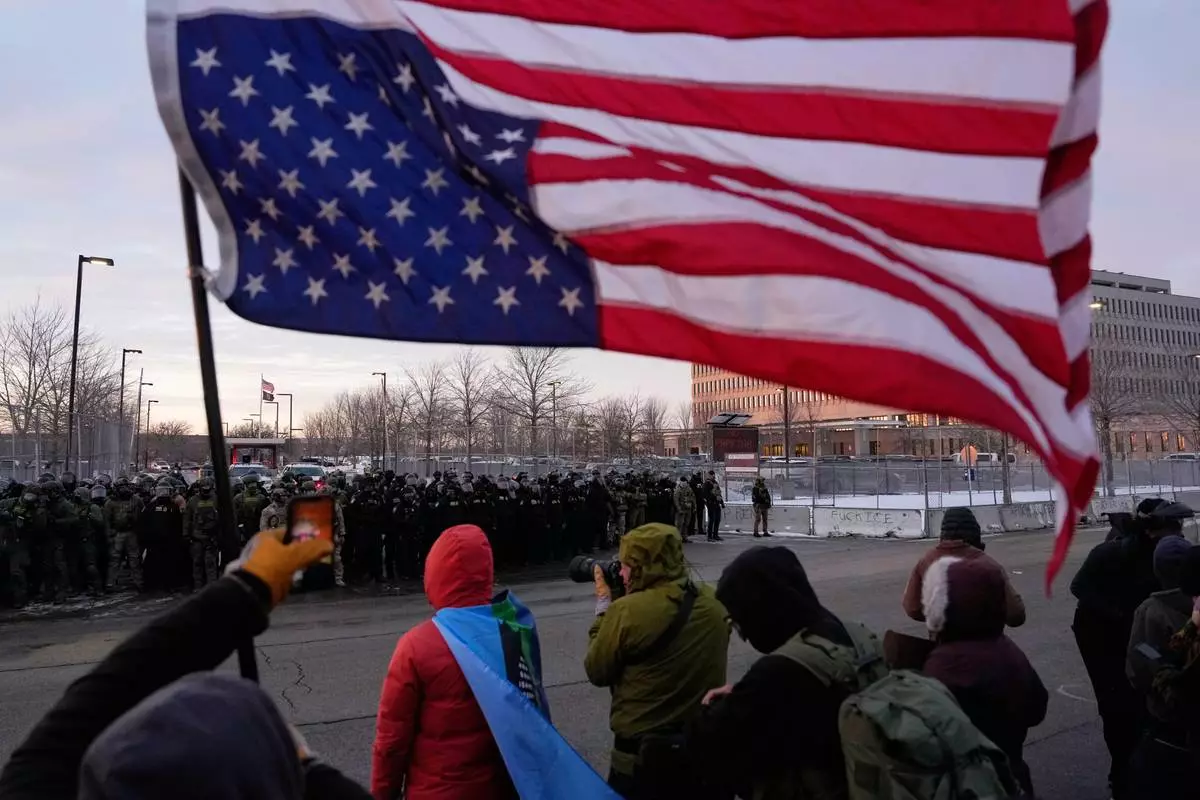 A person holds an upside-down American flag as law enforcement stand during a protest outside the Bishop Henry Whipple Federal Building on Saturday, Jan. 17, 2026, in Minneapolis. (AP Photo/Yuki Iwamura)