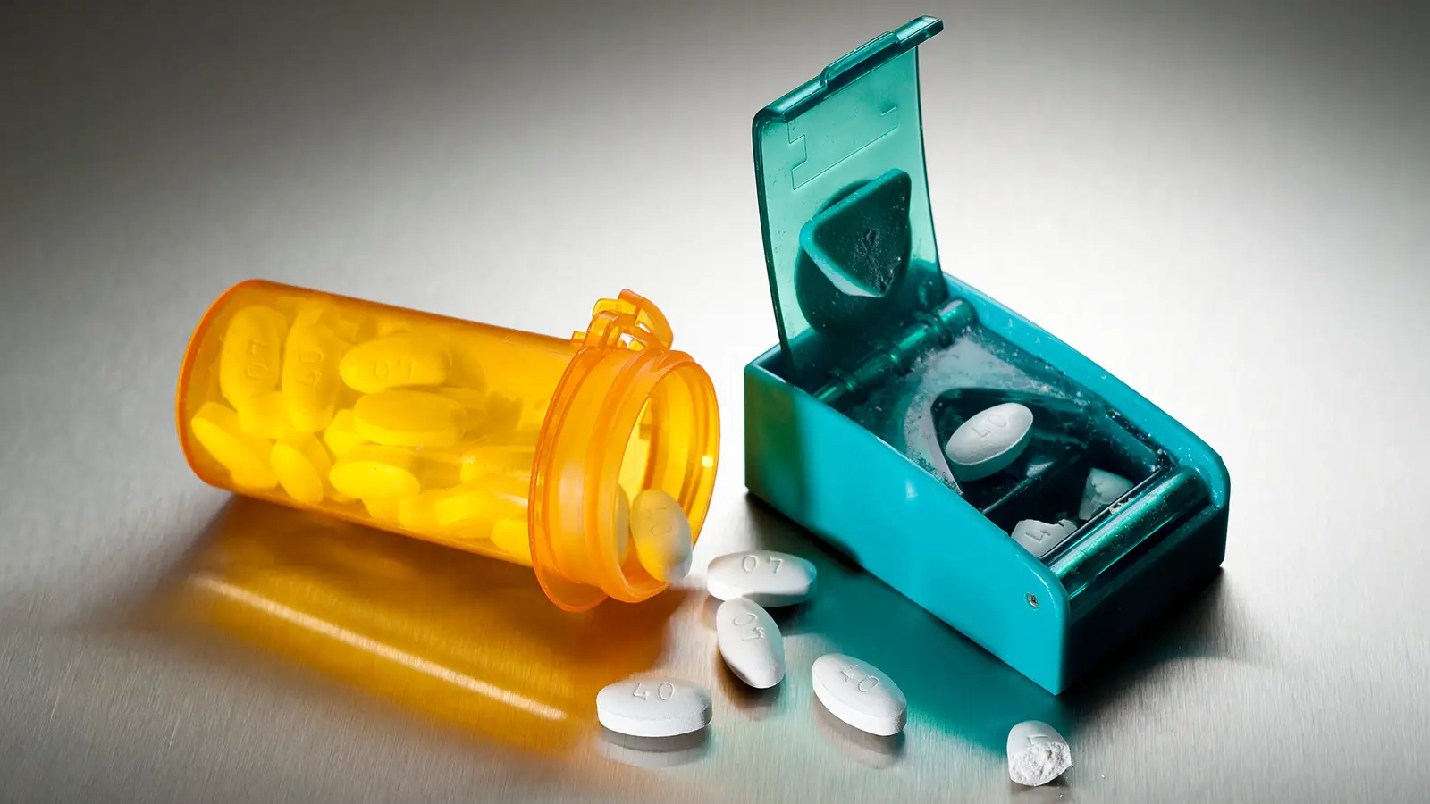 A photo of a pill cutter next to a spilled prescription medication bottle.