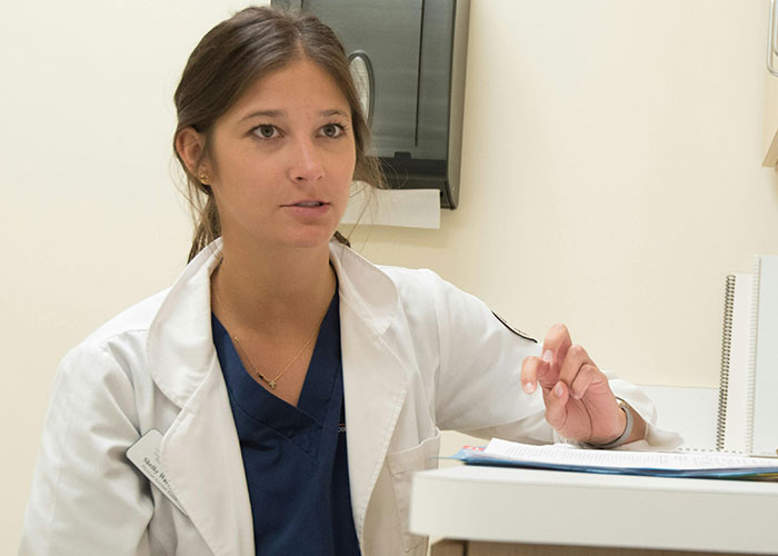 Female medical professional in a white coat discussing patient care and communication in a clinical setting.