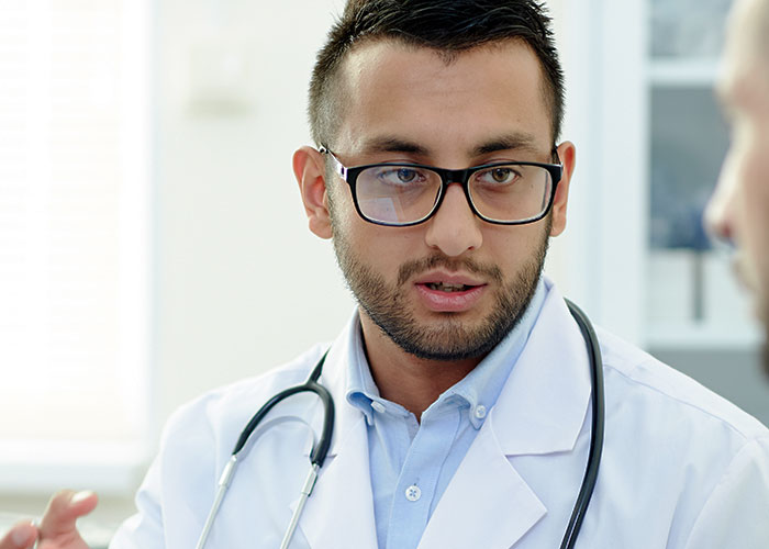 Young male doctor with glasses and stethoscope speaking seriously to a patient during a consultation about unprofessional remarks.