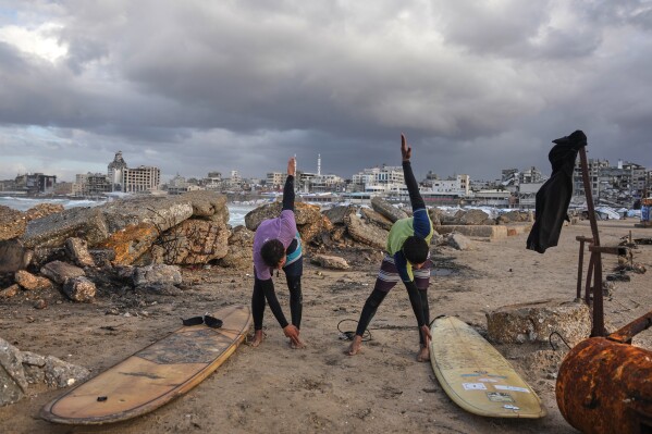 Palestinian Khalil Abu Jayyab, right, and Tahseen Abu Assi warm up before surfing on the beach in Gaza City, Dec. 28, 2025. (AP Photo/Jehad Alshrafi, File)