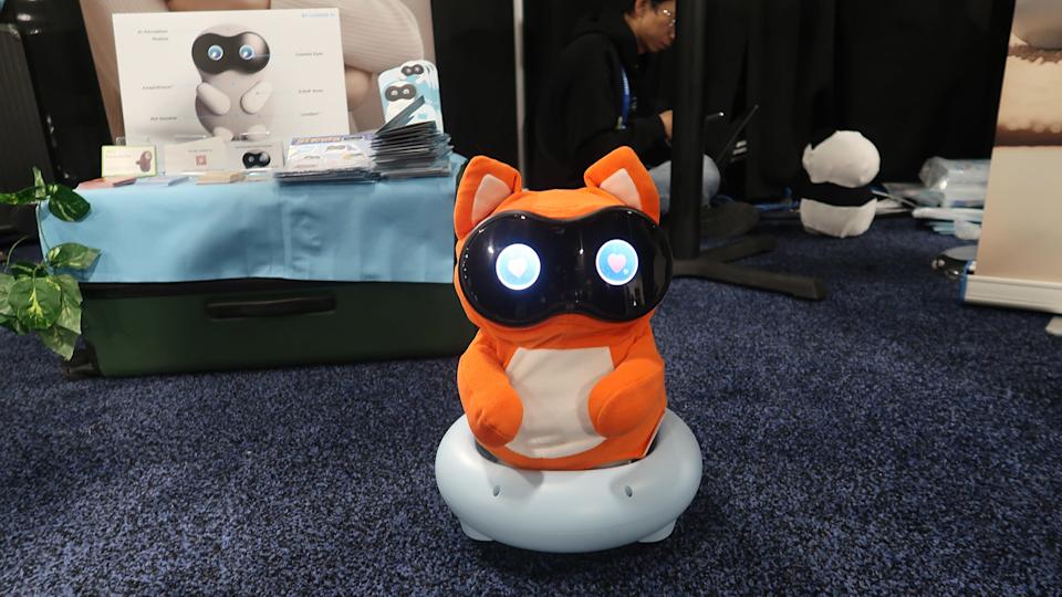 An orange, egg-shaped robot with a black face hearts in its eyes sitting on a wheeled base.