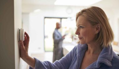 Mature Woman Turning Control Dial On Digital Central Heating Thermostat At Home.