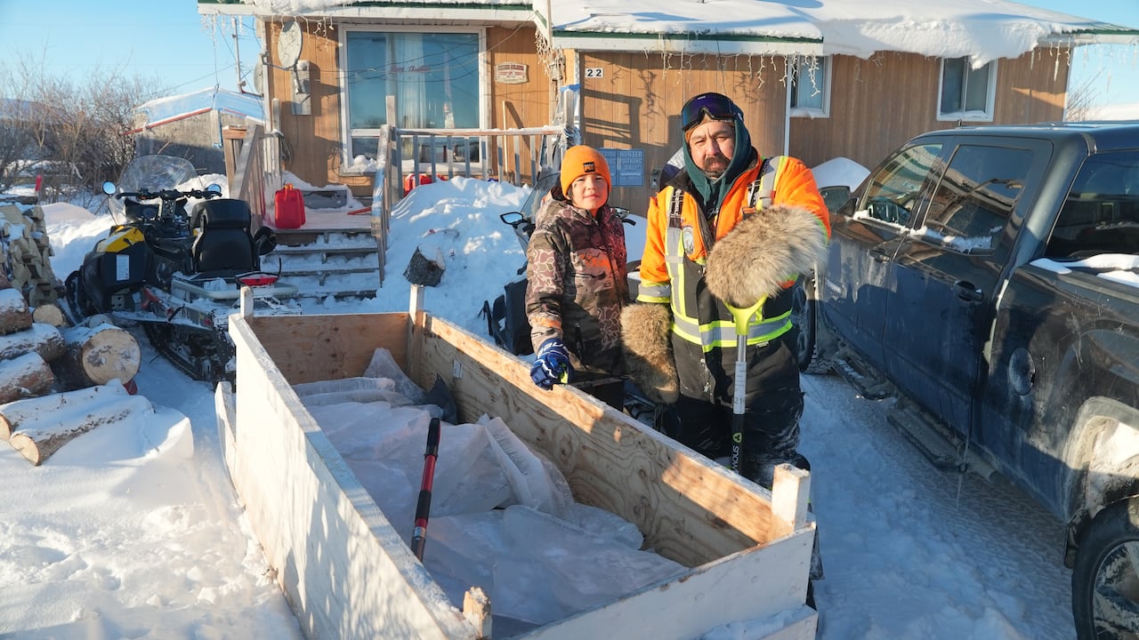 A man and boy standing next to a small trailer with big pieces of ice in it.