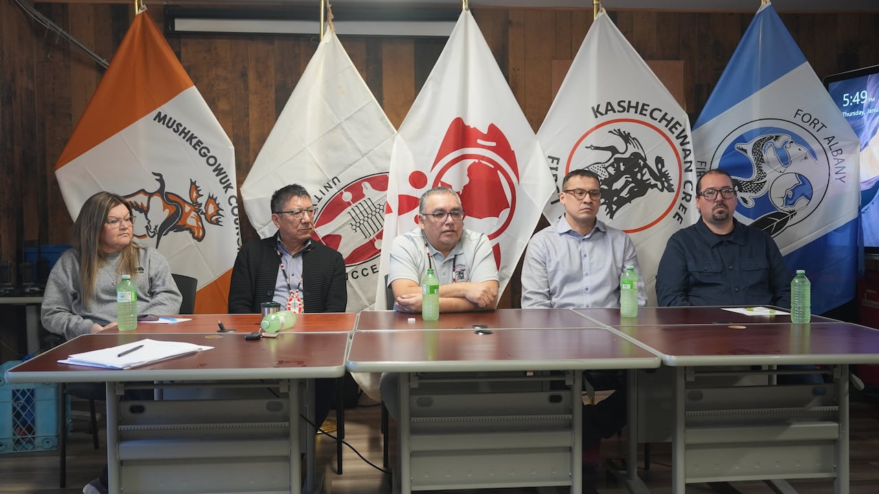 Five people sitting at a table with a flag behind them.