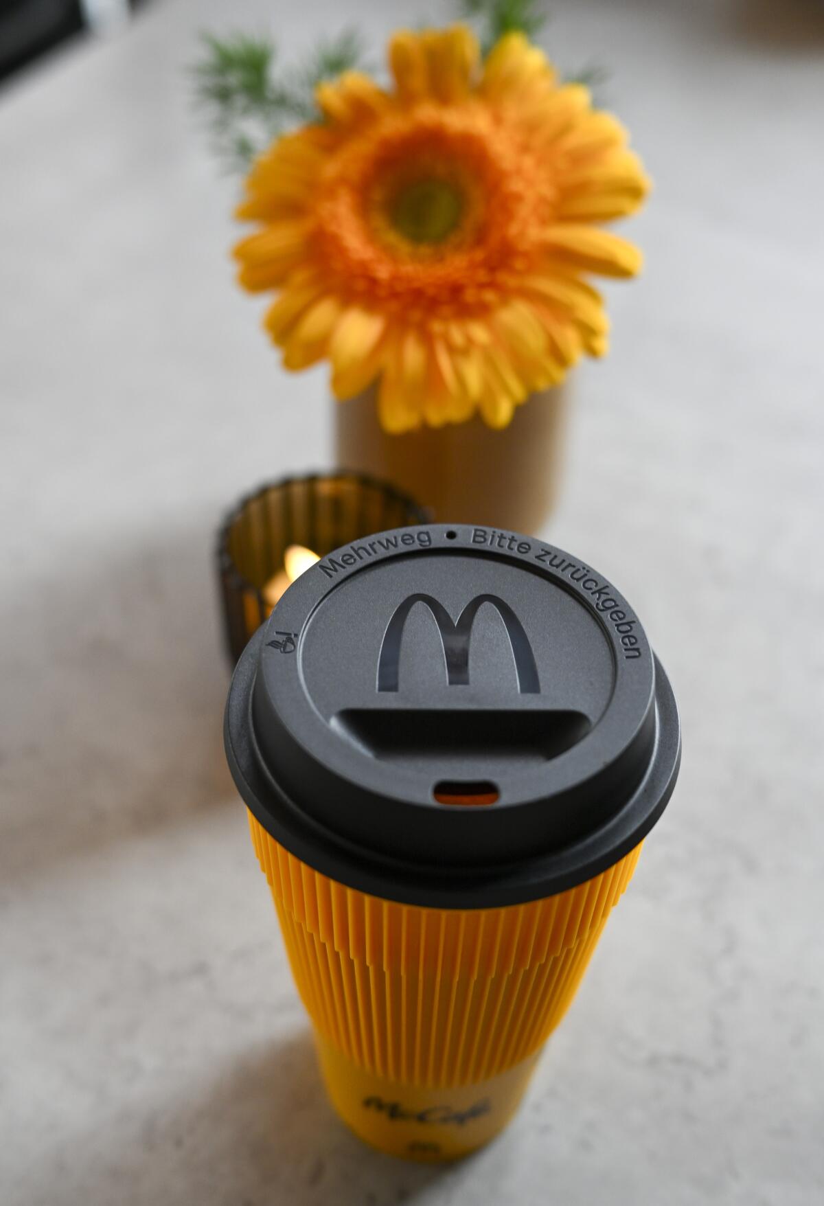 A reusable cup with a black lid next to an orange flower 