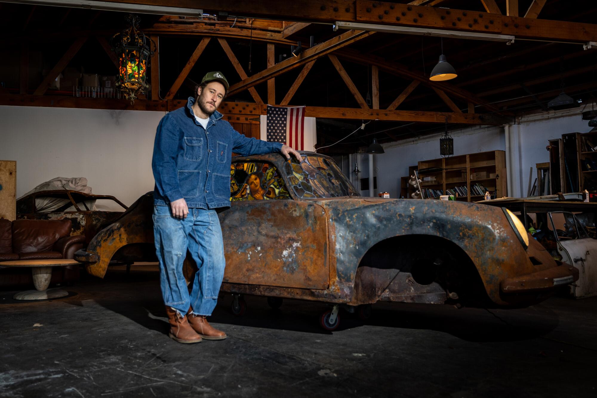 A man stands next to a piece of art made from a burned Porsche.
