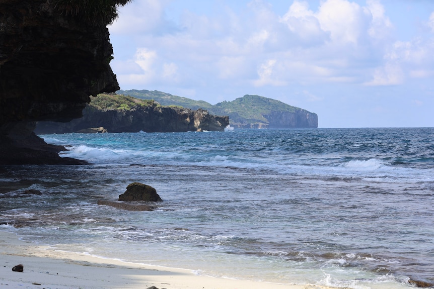 Shallow waves along a coastline with green forrest and sharp cliffs in the distance.