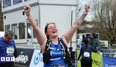 Alicia wearing a running bib and Bath Mind branded tank top with her hands in the air at the Bath Half Marathon finish line.