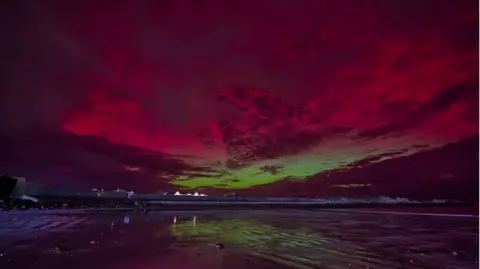 Martyn Torode A beach with green sand that is a reflection of what is in the sky. There are also reds and purples in the sky as well due to the Northern Lights 