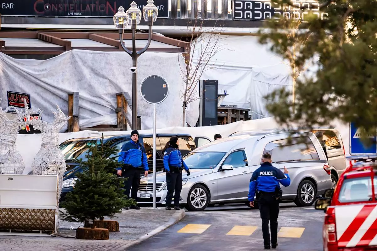 A hearse drives past as police officers inspect the area where a fire broke out at the Le Constellation bar and lounge during New Year's celebration, in Crans-Montana, Switzerland, Thursday, Jan. 1, 2026. (Jean-Christophe Bott/Keystone via AP)